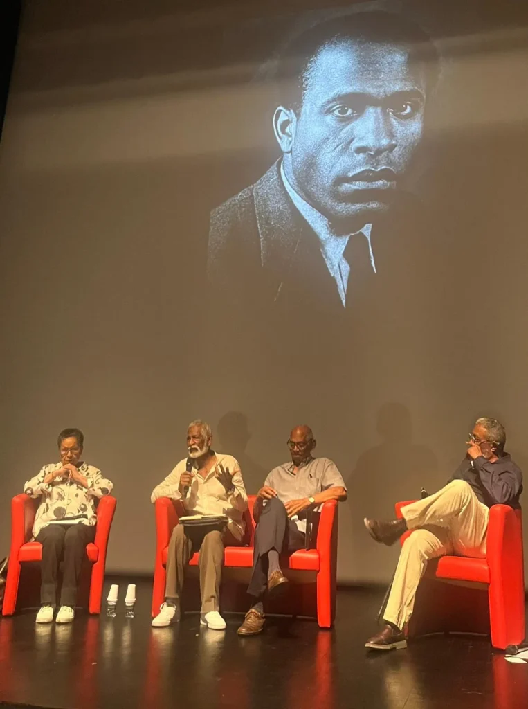 Quattro relatori antillani parlano con un'immagine di Frantz Fanon alle spalle